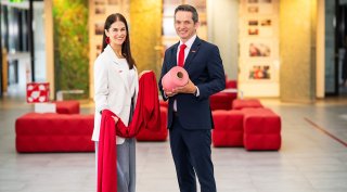 Im Bild v.l.n.r.: Eva-Maria Wurzer, Business Development Textilien Saubermacher; Andreas Opelt, CEO Saubermacher © 2026-kumpPhotography Eine Frau und ein Mann stehen in einem Unternehmensgebäude und präsentieren rote Textilien sowie eine rosafarbene Stoffrolle. © 2026-kumpPhotography