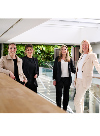 Your contact at Saubermacher's HR department – Photo credit: Saubermacher Four employees from the HR department stand together in a modern, light-filled office area with a green backdrop. The image conveys openness, professionalism, and personal support during the application process.