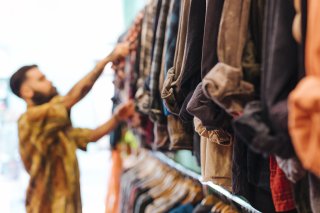 Kleidung bekommt ein drittes Leben © magnific.com Ein Mann durchsucht eine Kleiderstange mit gebrauchter Kleidung in einem Second-Hand-Laden. – © magnific.com