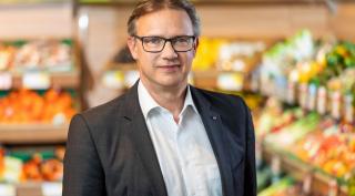 Christian Holzer, Spar Mann stehend vor einem Gemüseregal eines Supermarkts.